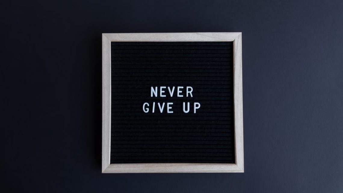 Inspirational letter board with 'Never Give Up' phrase on gray background.