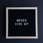 Inspirational letter board with 'Never Give Up' phrase on gray background.