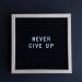Inspirational letter board with 'Never Give Up' phrase on gray background.